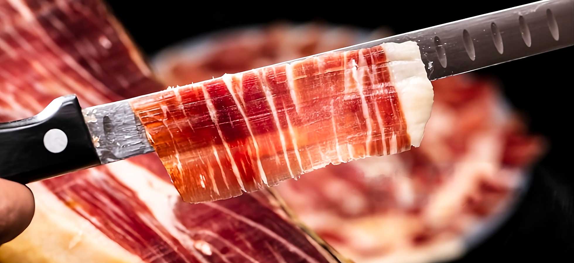 Primer plano de una loncha de jamon ibérico recien cortado con un cuchillo jamonero.