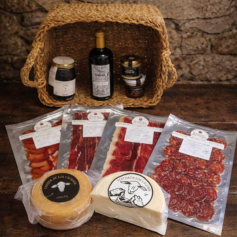 Cesta de mimbre con embutidos ibéricos al vacío, cuñas de queso, aceite y miel.
