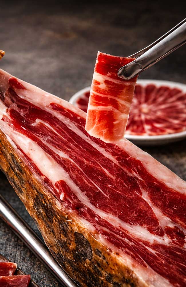 Detalle de pinzas sujetando una loncha de jamón ibérico recién cortado, sobre un jamón.